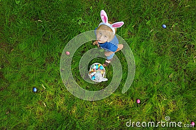 Aerial view of little boy wearing bunny ears costume hunting for eggs in spring garden on Easter day. Point of drone view. Stock Photo