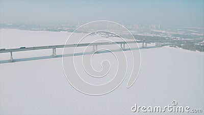 Aerial view of a long bridge above snow and ice covered river between two parts of a city. Clip. Winter landscape with a Stock Photo