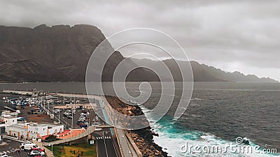 Aerial view of the promenade and coastal stones in the port city of Agaete. Giant misty rocks hanging over the dark Stock Photo