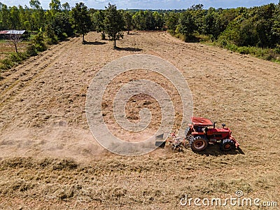 Aerial view of Tractor as pulling round baler, machine that rolls up the straw and spits out a packed bale over agricultural field Stock Photo
