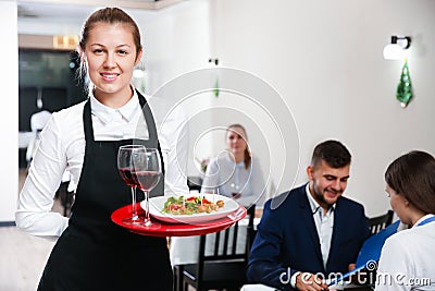 Affable female waiter is standing with order in luxury restaurante Stock Photo