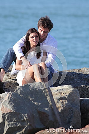 Affectionate couple flirting and hugging on a stone on the beach Stock Photo