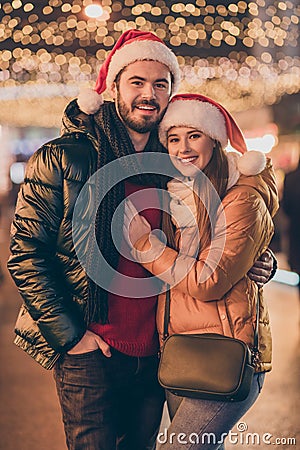 Affectionate jolly couple hugging on x-mas fair under evening outside tradition lights wear winter coats santa claus Stock Photo