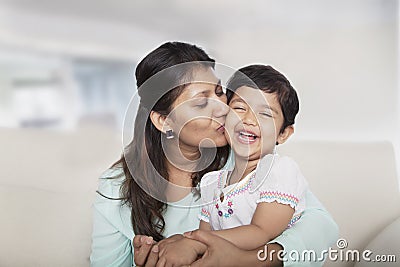 Affectionate mother holding and kissing her daughter on the couch Stock Photo