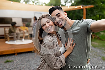 Affectionate multiracial couple taking selfie near RV, resting with their friends outdoors, copy space Stock Photo