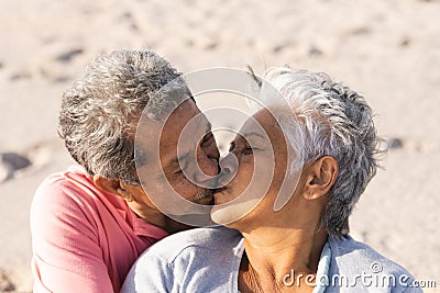 Affectionate multiracial senior couple kissing on lips while enjoying sunny day at beach Stock Photo