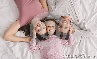 Affectionate Parents And Little Daughter Lying Together In Bed, Top View Stock Photo