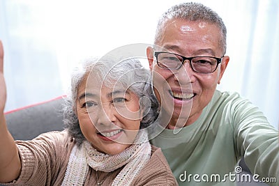 Affectionate senior Asian couple sharing warm embrace on the sofa, celebrating their enduring love and togetherness. Elderly Stock Photo