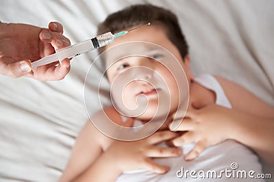 Afraid fat little child lies on a background of hand with a syringe and looking at it Stock Photo