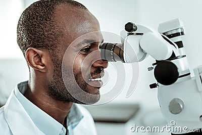 African American beaming stomatologist actively working with microscope Stock Photo