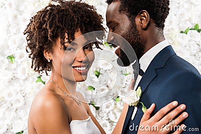 African american bride hugging handsome bridegroom near flowers Stock Photo