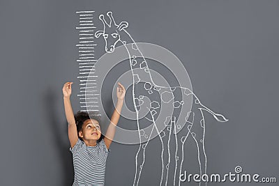 African-American child measuring height near chalk giraffe drawing on grey Stock Photo