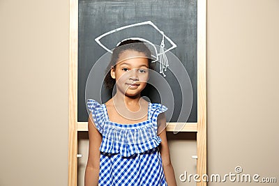 African-American child standing at blackboard with chalk drawn academic cap. Education Stock Photo