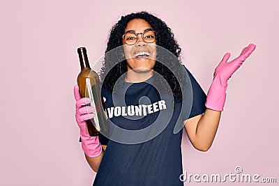 African american curly woman wearing volunteer t-shirt doing volunteering recycling glass bottle very happy and excited, winner Stock Photo
