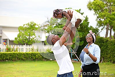 African American family playing with young happy little daughter on green grass field while enjoying summer garden Stock Photo