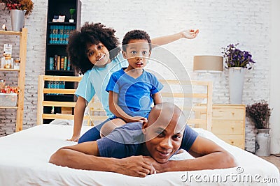 African American family of three, kids sitting on father`s back at home Stock Photo