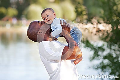 African American father kisses, holds on arms and loves child son mixed race outdoors in summer Stock Photo