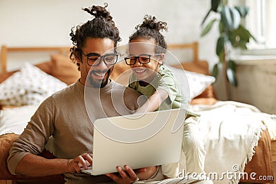 African american father with little son sitting in bedroom at home with laptop and watching cartoons Stock Photo