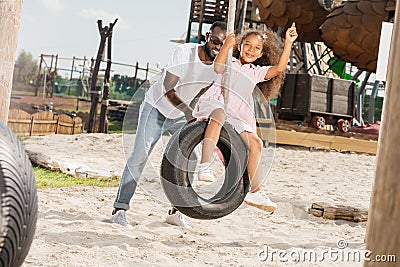african american father pushing daughter on tire swing Stock Photo