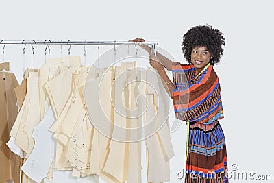 African American female designer with sewing patterns on clothes rack over gray background Stock Photo