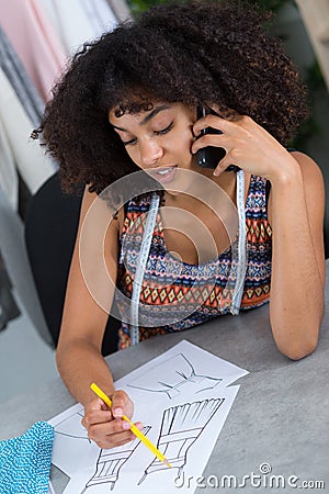 African american female dressmaker sketching design and talking on telephone Stock Photo