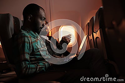 African american freelancer working on laptop during sunset flight Stock Photo