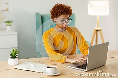 African american girl using laptop at home office looking at screen typing chatting reading writing email. Young woman Stock Photo