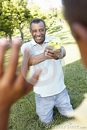 African American Grandfather And Grandson Playing With Water Pistols In Park Stock Photo