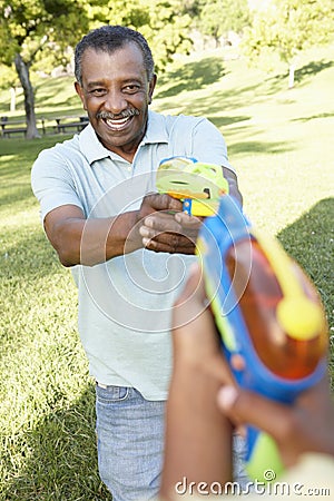 African American Grandfather And Grandson Playing With Water Pistols In Park Stock Photo