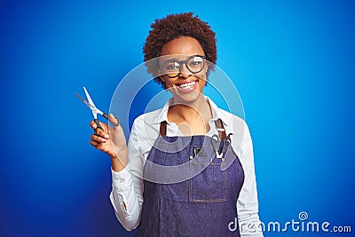 African american hairdresser woman holding scissors over blue isolated background with a happy face standing and smiling with a Stock Photo