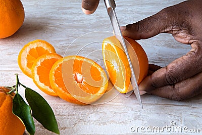 African American Male Hand slicing oranges on white marble tray. Healthy Citrus Fruit Stock Photo