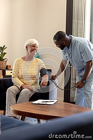 African american male health worker checking blood pressure of caucasian senior woman at home Stock Photo