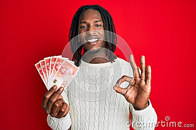 African american man with braids holding 20 israel shekels banknotes doing ok sign with fingers, smiling friendly gesturing Stock Photo