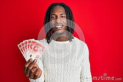 African american man with braids holding 20 israel shekels banknotes looking positive and happy standing and smiling with a Stock Photo