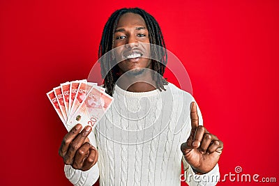 African american man with braids holding 20 israel shekels banknotes smiling with an idea or question pointing finger with happy Stock Photo