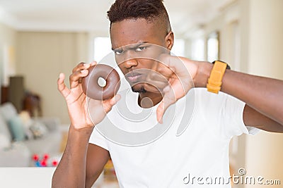 African american man eating chocolate donut with angry face, negative sign showing dislike with thumbs down, rejection concept Stock Photo