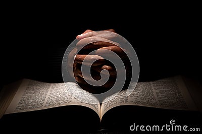 African American Man Praying with Hands on Top of the Bible Stock Photo