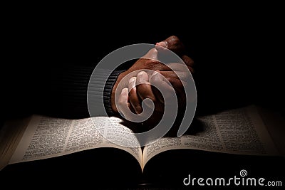 African American Man Praying with Hands on Top of the Bible Stock Photo