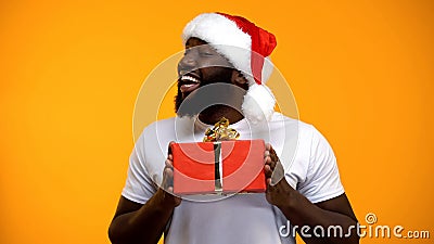 African-American man in Santa hat presenting Christmas gift, yellow background Stock Photo