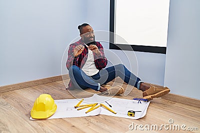 African american man sitting on the floor at new home looking at blueprints disgusted expression, displeased and fearful doing Stock Photo