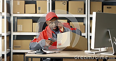 African American man talking on mobile phone while working at post office store and on computer. Postman scanning bar Stock Photo