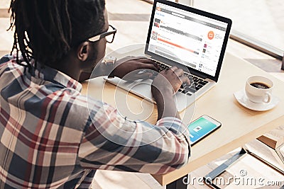 african american man using laptop with soundcloud website and smartphone Editorial Stock Photo