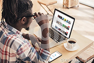 african american man using laptop with youtube website and smartphone Editorial Stock Photo