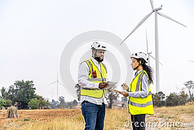 African american man and woman engineers in uniform discuss and use tablet working stand near wind turbines ecological energy Stock Photo