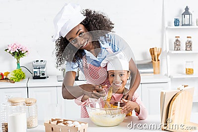 african american mother and daughter in chef hats mixing dough with whisk Stock Photo