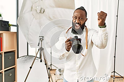 African american photographer man working at photography studio angry and mad raising fist frustrated and furious while shouting Stock Photo