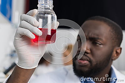 African American Scientist Examine Flask With Red Luquid Working In Modern Laboratory, Male Researcher Making Experiment Stock Photo