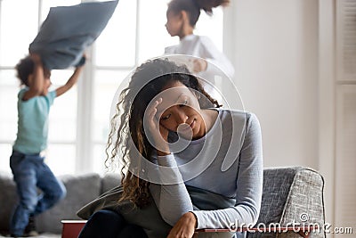 African mom feels tired of noisy children playing at home Stock Photo