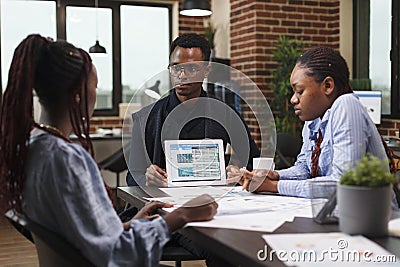 African american team leader presenting to research team financial statistic data on tablet. Stock Photo