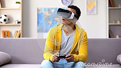 African-American teen boy with joystick playing video game in VR headset, future Stock Photo